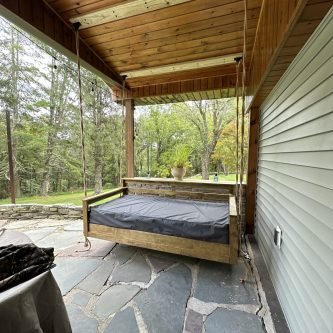 Swing bed on a covered porch with stone flooring, surrounded by trees, showcasing outdoor living space in Northeastern Pennsylvania.