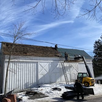 Roofing professionals replacing shingles on a barn-style building in winter, showcasing E-Stern Construction's expertise in roof replacements in the Wilkes-Barre area.