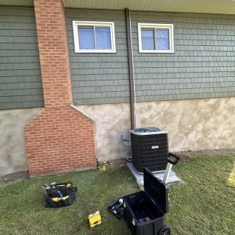 Home exterior with green siding, brick chimney, and air conditioning unit, showcasing recent home improvement work by E-Stern Construction in Wilkes-Barre, PA.