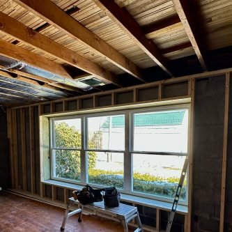 Interior renovation in progress showcasing a large window framed with wooden beams, tools on a ladder, and a view of the exterior garden, reflecting E-Stern Construction's home improvement services.