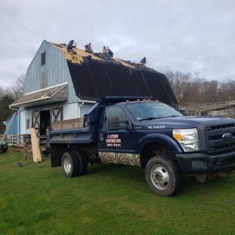 E-Stern Construction truck parked in front of a barn with workers replacing the roof, showcasing roofing services in Northeastern Pennsylvania.