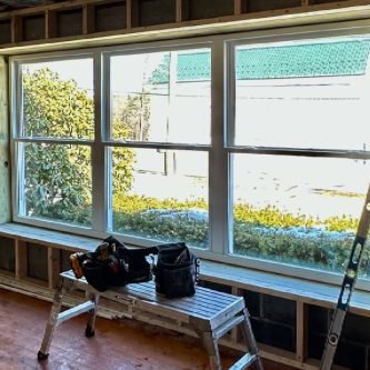 Newly installed large replacement windows in a home renovation, showcasing a view of the outdoors with tools and a ladder nearby, emphasizing E-Stern Construction's home improvement services in Wilkes-Barre, PA.